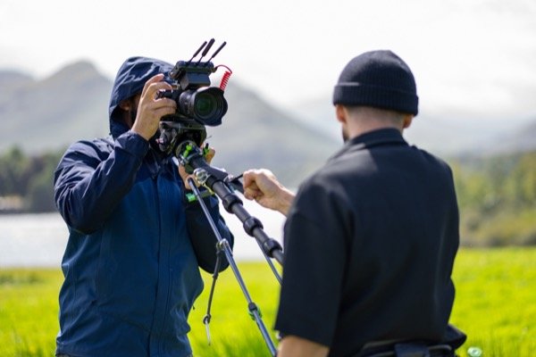 Cinematographer setting up camera on tripod for outdoor shoot with mountain backdrop
